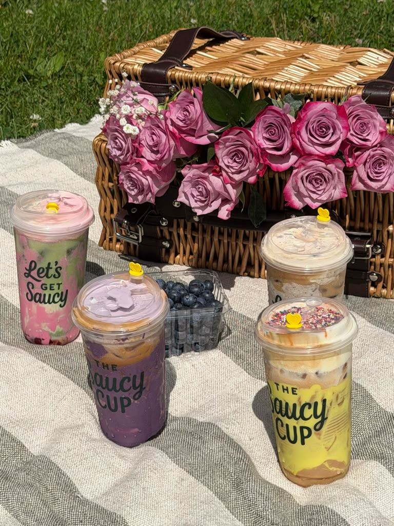 Four Saucy Cup drinks on a picnic blanket with roses